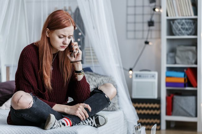 Drug Slang and Warning Signs - young red haired girl sitting on bed talking on cell phone