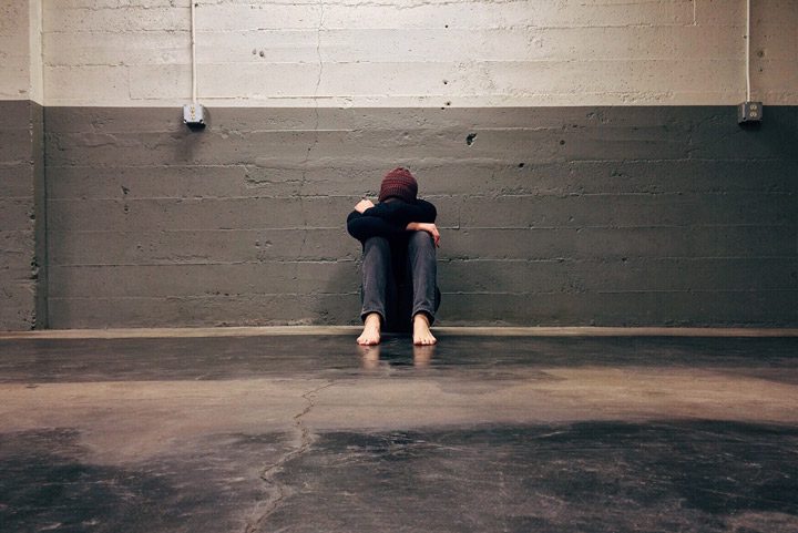 person leaning against wall with head and arms on knees - opioid addiction