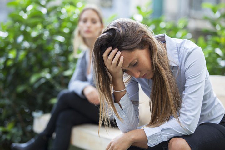 two women sitting outside, one is upset with head on hand - relapse