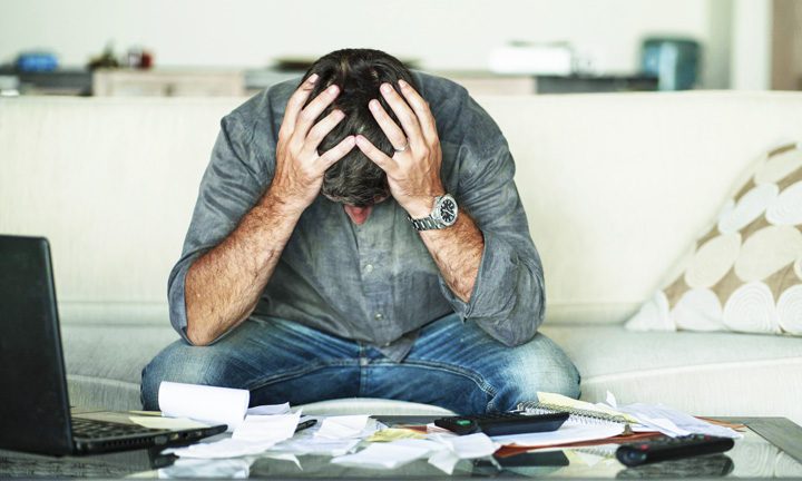 stressed out man with head in hands surrounded by papers - financial