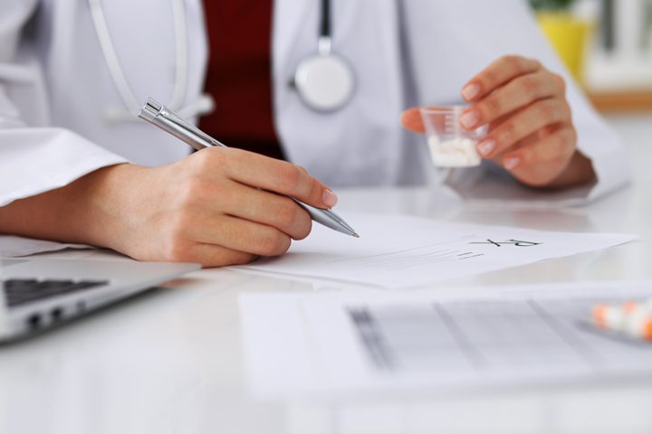 doctor writing prescription and holding cup of pills - professionals treatment program