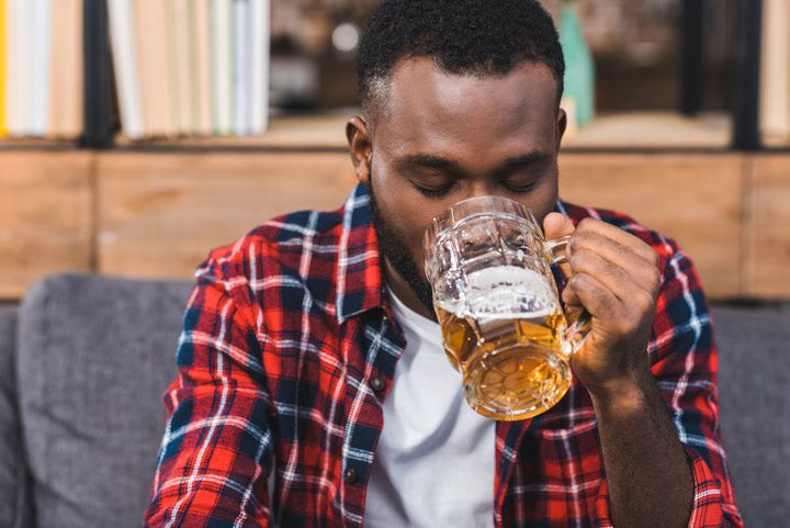 young African American man in plaid shirt drinking a beer from a glass mug - alcohol detox