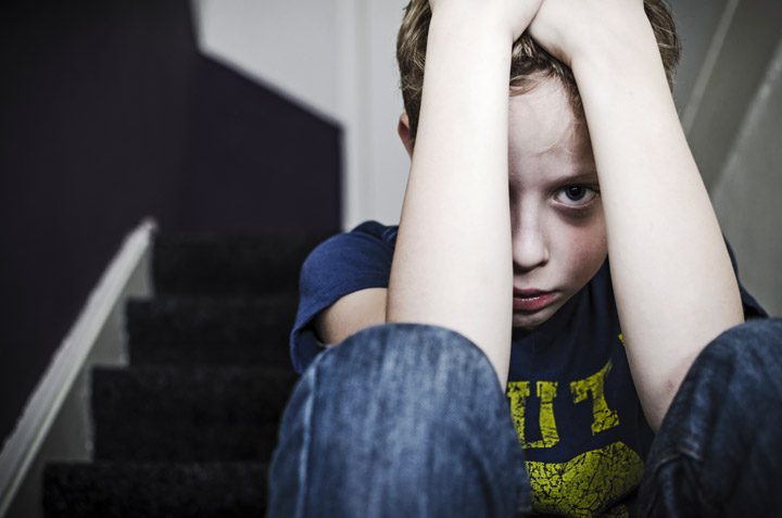 sad little boy sitting on steps with arms covering most of his sad face - past trauma, childhood trauma