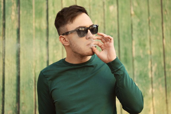 young adult man in green sweater and sunglasses smoking a marijuana joint - marijuana addiction