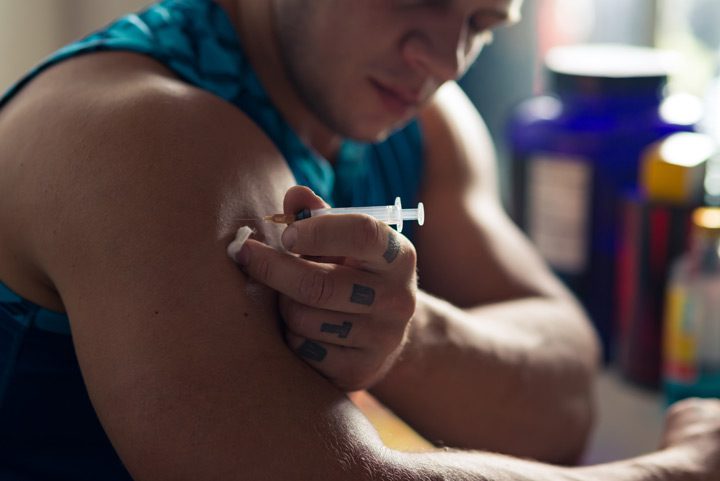 young man using a syringe to inject anabolic steroids into his shoulder